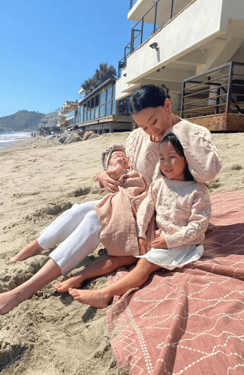 asian mom with baby and toddler girl wearing matching cute fisherman pullover sweaters by the beach