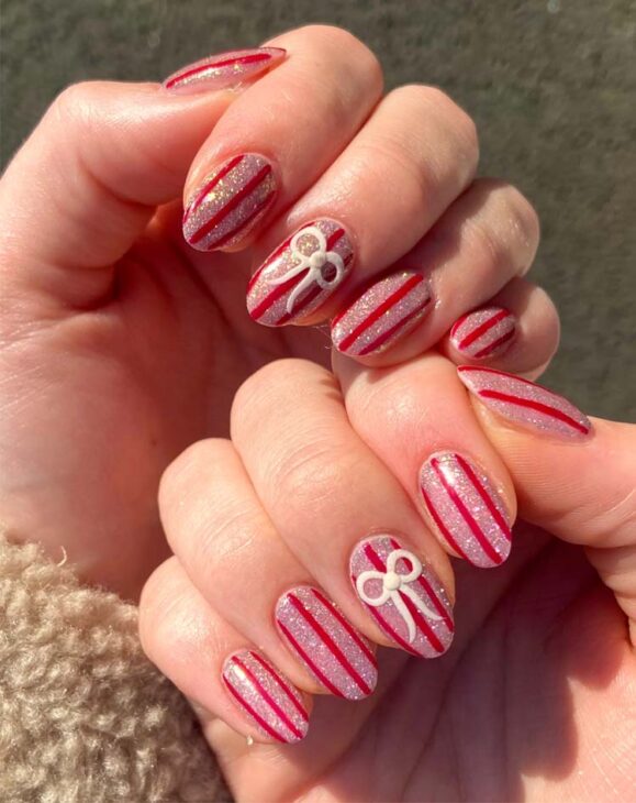 glittery pink and red stripe christmas almond nails with white bow design