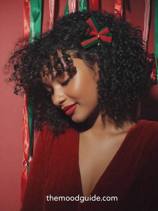 curly and cute christmas hair down hairstyle aesthetic idea on medium size hair with small red and green bow clip